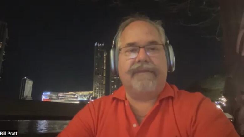 A man in a red shirt at night with buildings in the background. 