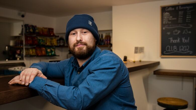 A man with a beard and toque sits at a bar.