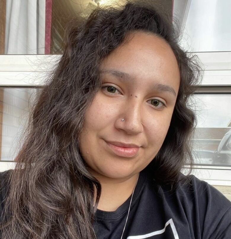 Latanya Tait is described as a five-foot-seven Indigenous woman with a medium build, medium-length brown curly hair, and brown eyes. In this photo she is grinning while looking at the camera. 