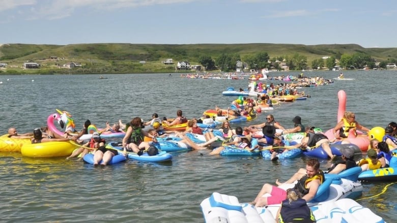 A line of floaties with people on them stretches out across a lake. 