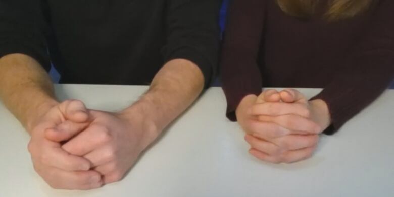 A man and woman's hands and arms resting on a table.