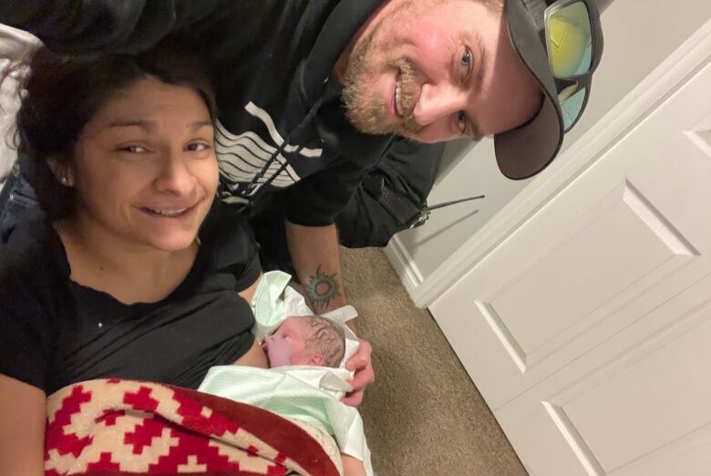 A smiling woman holds a newborn baby as he breastfeeds, with the father smiling next to them.