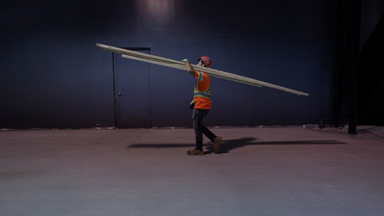 A construction worker carries long beams on his shoulder. 