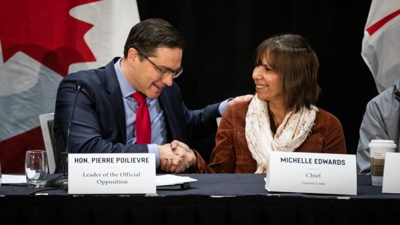 Two politicians seated at an announcement on stage.