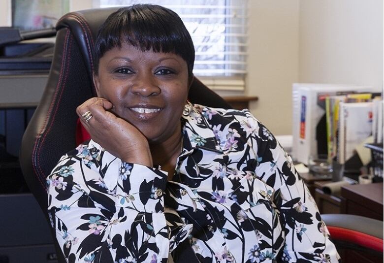 A woman in a patterned shirt sits in an office chair.