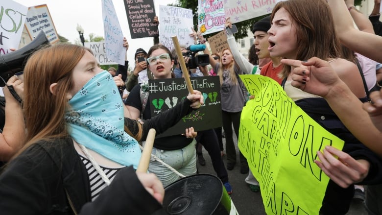 Protesters holding pro-choice and anti-abortion signs shout at each other.