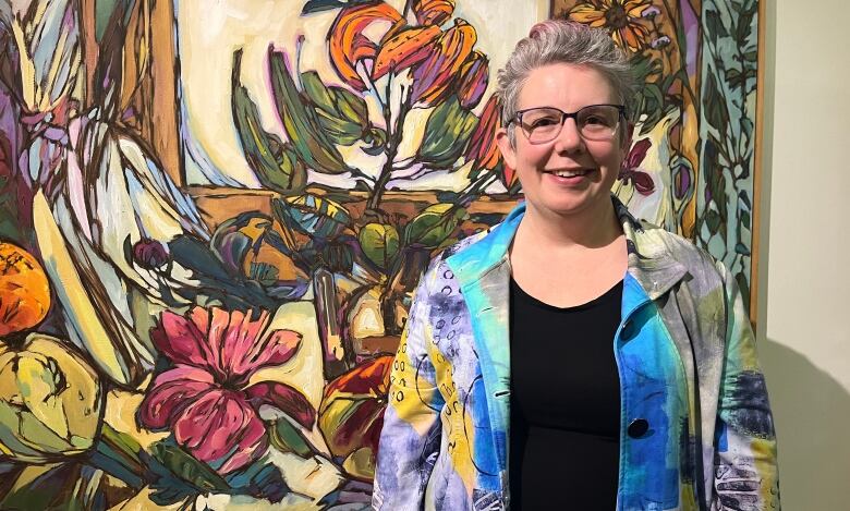 A woman in a colourful blazer stands in front of a painting. 