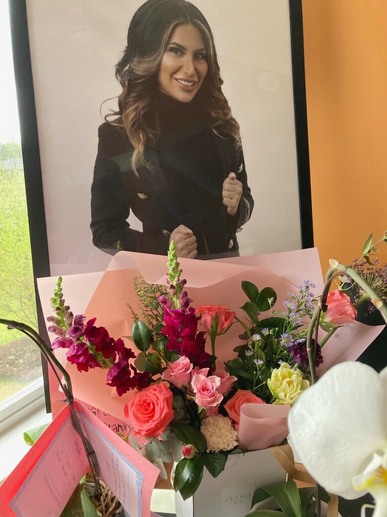 A photo of a young woman in professional attire stands behind a bouquet of funerary flowers.