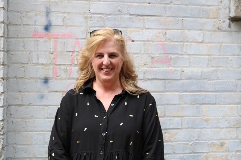 A portrait of woman wearing a black blouse in front of an old, white brick wall.