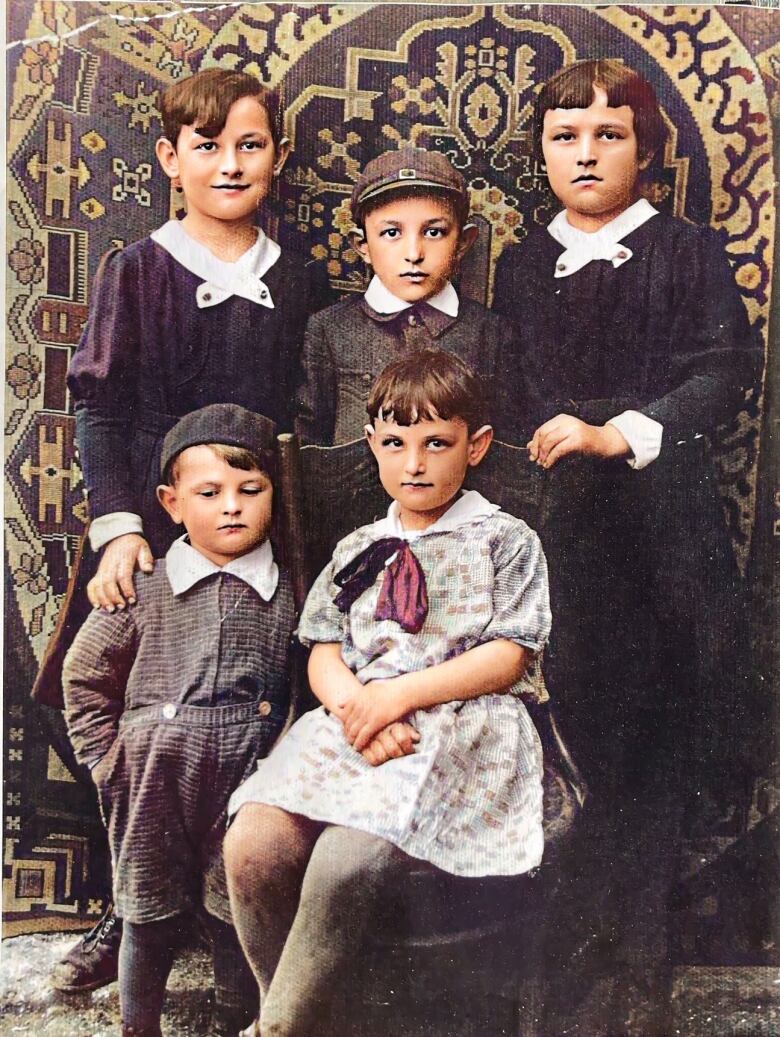 A black and white photograph shows five children -- two in the front row and three behind -- all looking at the camera.