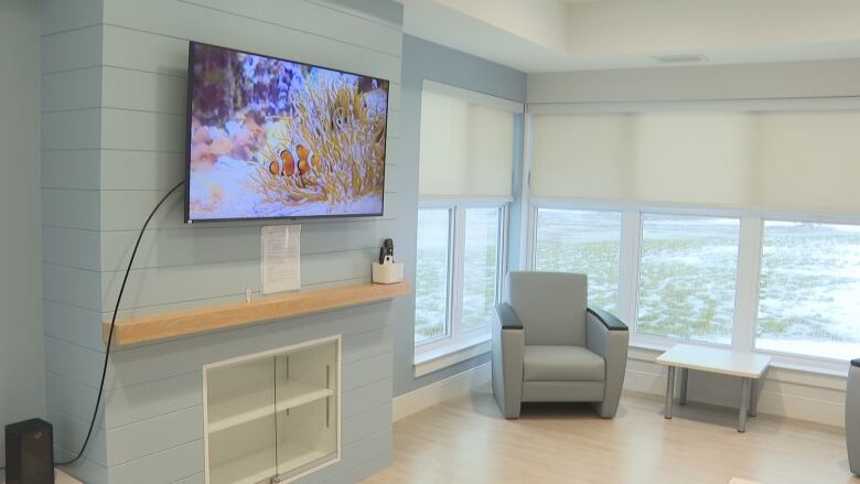 View of room with cushioned chair, side table and large windows.