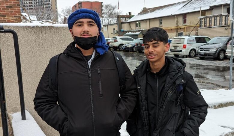 Two students stand with their hands in their winter coats