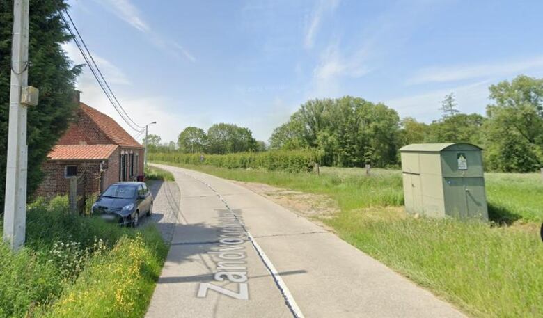 A country road in Belgium, with a forested area to the centre-right of the road.