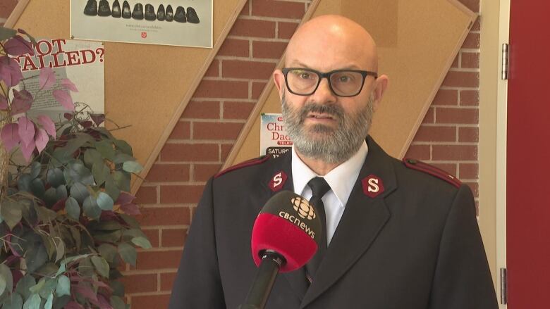 A bearded man with glasses dressed in a Salvation Army uniform stands in front of a mic.