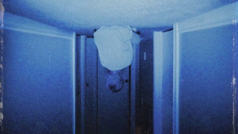 A grainy, black poorly lit photo shows a small child facing away from the camera. He is upside down, sitting on a hallway ceiling. 