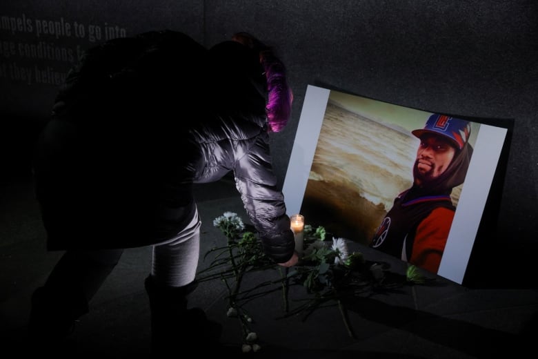 A woman leaves a flower at a photo of a person during a vigil.