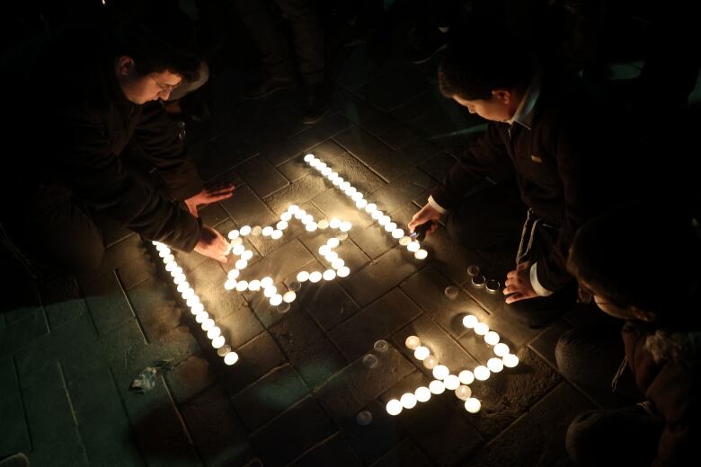 People at a vigil light candles arranged to look like Israeli flag and the number 7.