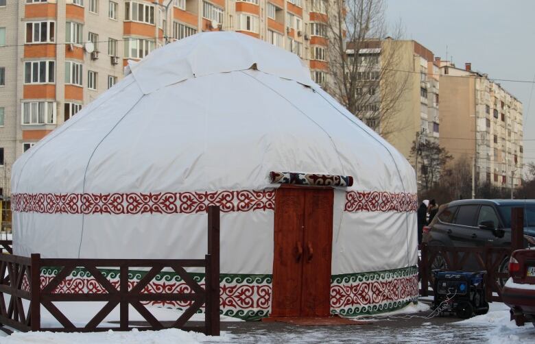 A yurt is shown near apartment buildings surrounded by snow.