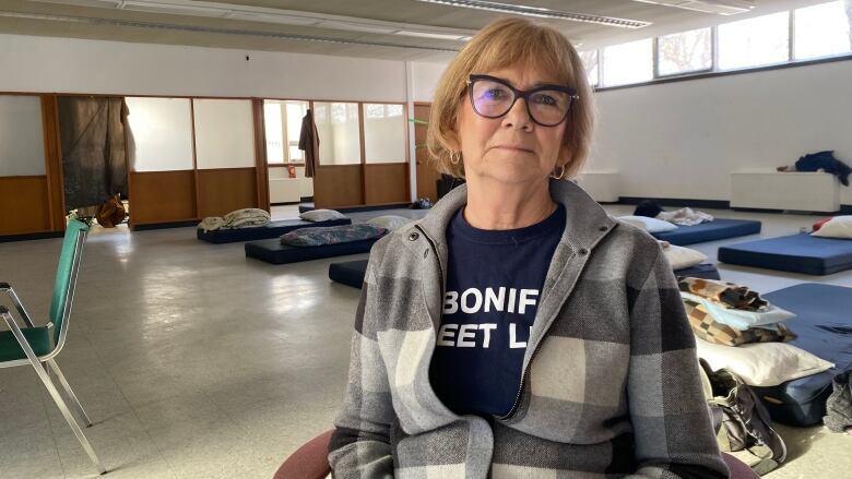 A woman seated in a chair, in front of beds at a warming shelter in Winnipeg.