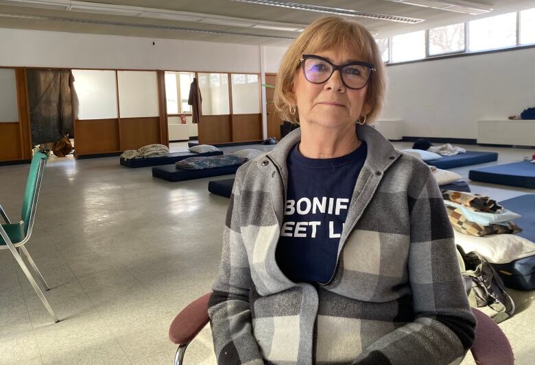 A woman seated in a chair, in front of beds at a warming shelter in Winnipeg.