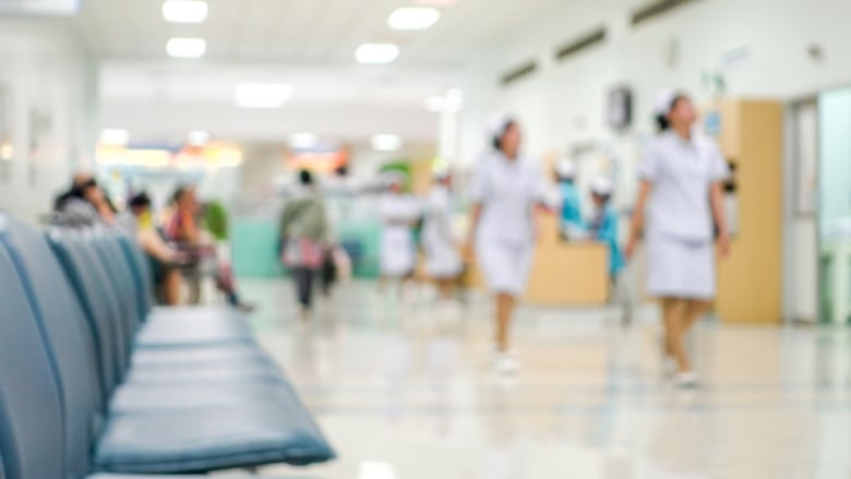 A photo shows the waiting room of a hospital with nurses blurry in the background. 