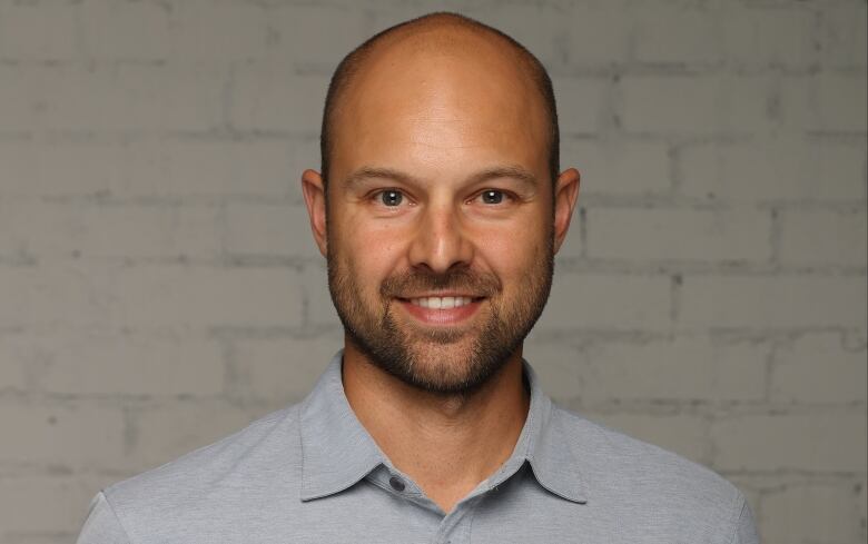 A headhost of a bald man with a light beard smiling. He is wearing a blue dress shirt. 