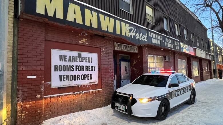 A police car is parked on a snowy sidewalk in front of a hotel.