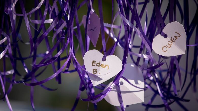 Purple paper hearts with names written on them hang on a fence in Vancouver.