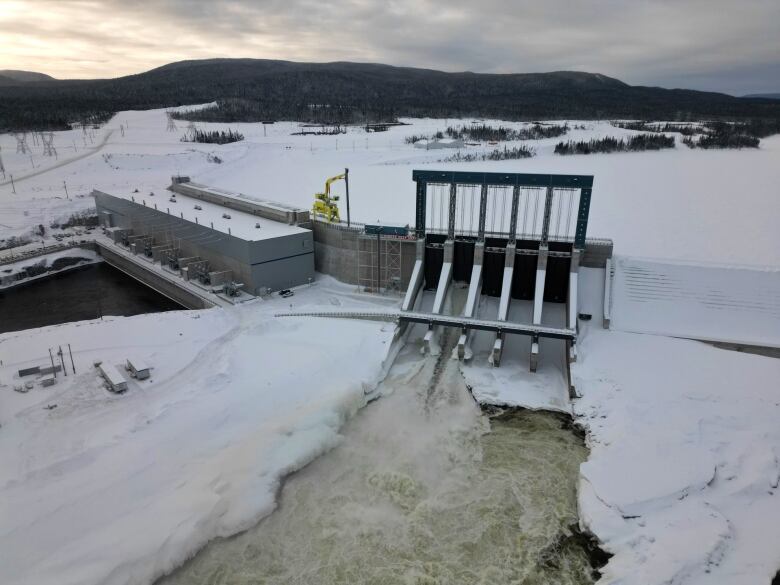 Water pours through the spillgates of the Muskrat Falls dam, whose reservoir is iced over and covered with snow.