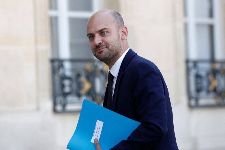 A man in a suit walks with a folder under his arm. 