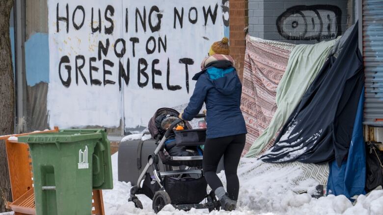 A woman pushes a stroller past the shelter of an unhoused person in Toronto on Tuesday, Jan. 31, 2023 as the coldest weather in years arrives. A precedent-setting legal ruling in Kitchener, Ontario on the eviction of unhoused encampments will see a wave of legal challenges starting in other cities, experts say. THE CANADIAN PRESS/Frank Gunn