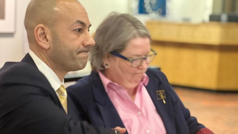 Man in suit holding hand of woman in suit, pink shirt.