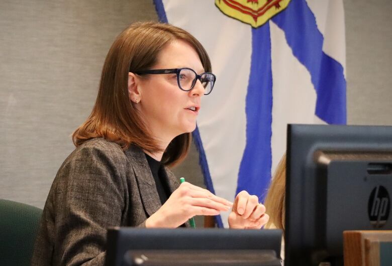 A woman speaks and gestures with a Nova Scotia flag in the background.