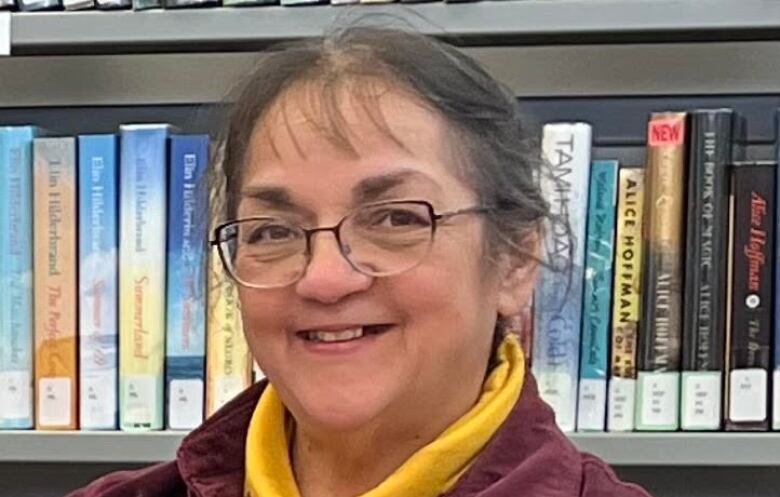 A woman with glasses stands before a bookshelf.