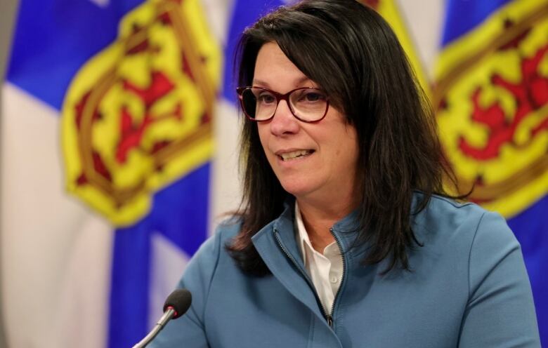 A woman with dark hair and glasses sits at a podium.