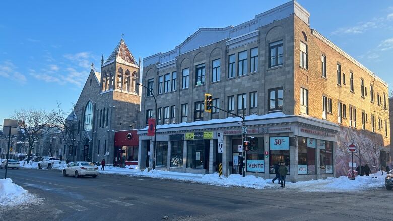 Snowing intersection, greystone building with shops on groundfloor.