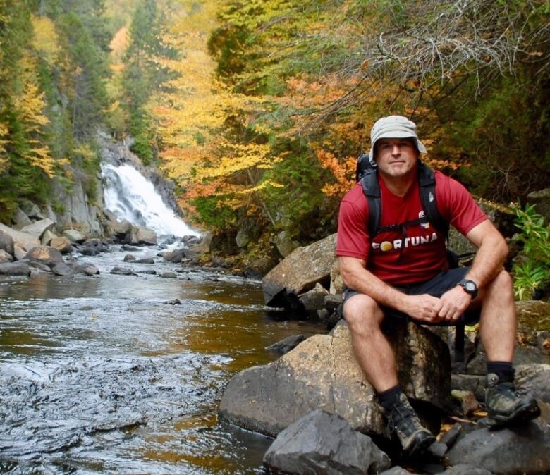 A man sitting by a stream and waterfall, in hiking gear.