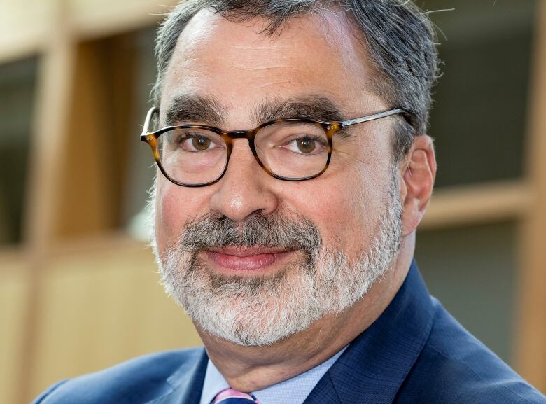 A man in a blue suit and glasses looks at the camera.