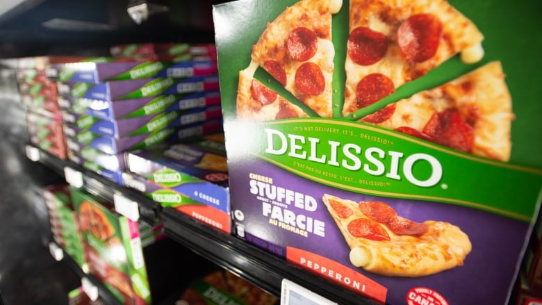 Green and purple boxes of frozen pizza stacked in a freezer.