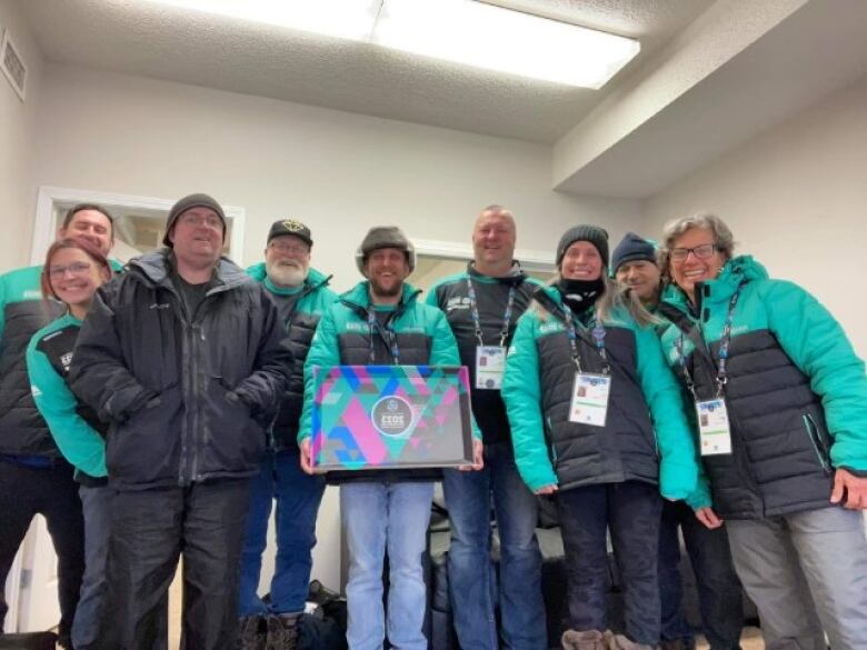 A group of nine volunteers pose while wearing Arctic Winter Games jackets. 