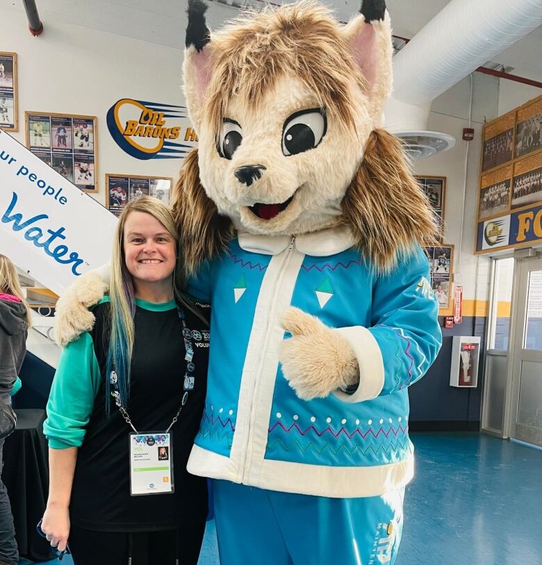 Melanie Bellows stands with Nitotem the lynx mascot, who is giving a thumbs up. 