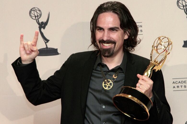 A man in a black suit holds up a golden trophy for winning a Grammy award.