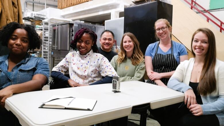 Six entrepreneurs smiling around a table, share a kitchen space