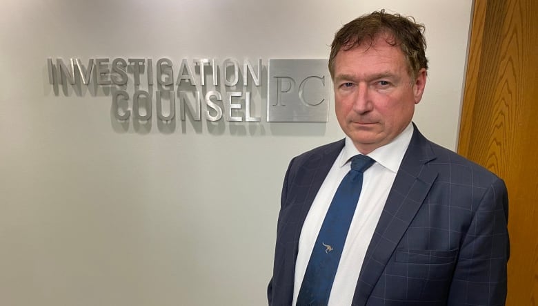 A man stands in front of a wall with the name of his law firm written on it.