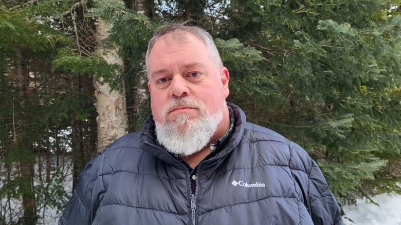 A man wearing a puffy dark blue coat standing in front of a row of trees