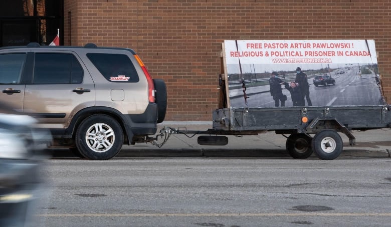 a car pulls a banner that reads 'free artur pawlowski, religious and political prisoner in canada'