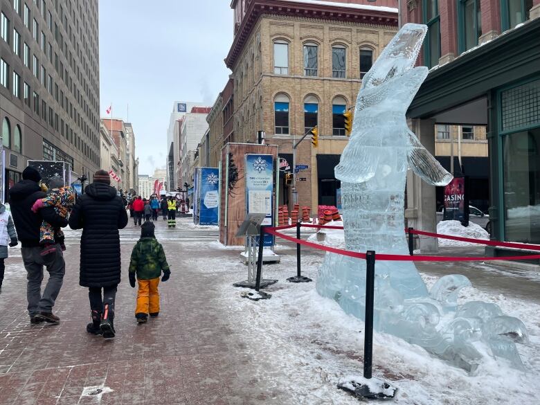 People walk on a city pedestrian street in winter next to a ice sculpture of a large fish.