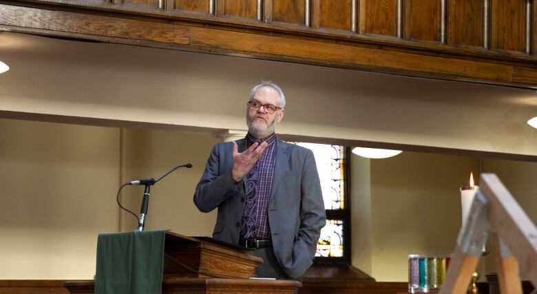 A man stands and speaks in front of a podium.