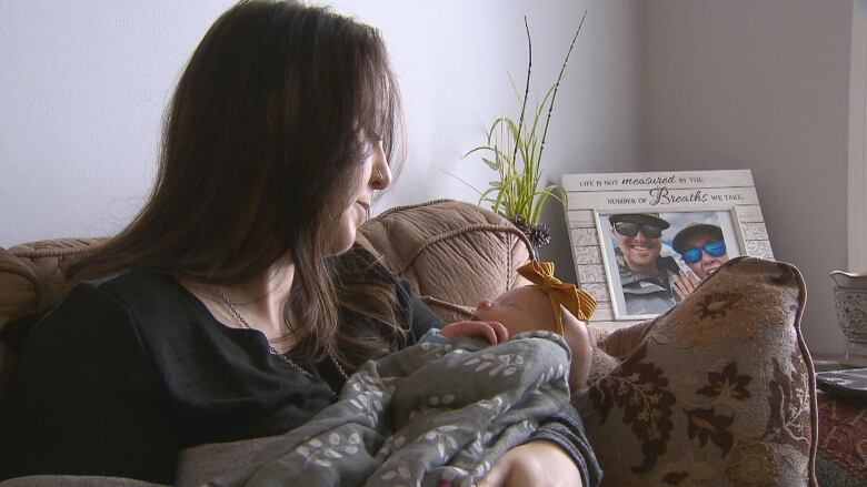 a woman with brown hair holds a tiny baby wearing a little yellow bow on its head