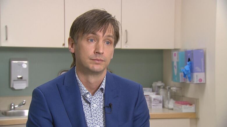 a man wearing a blue suit sits in a doctors office 